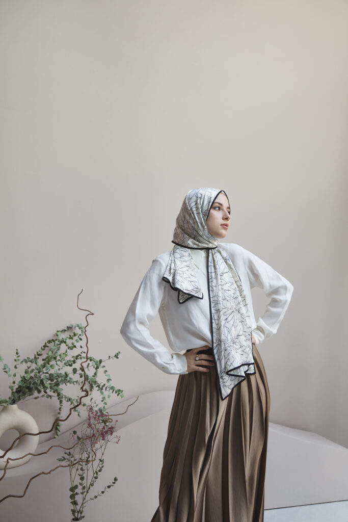 Femme portant une tenue mode modeste élégante avec hijab imprimé, chemise blanche et jupe plissée
